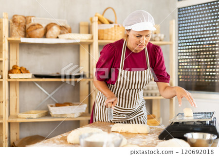 Female cook is working with dough, weighing piece of dough on scale. 120692018