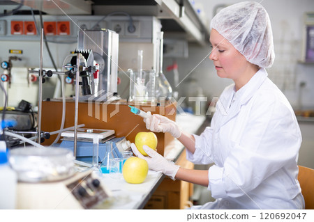 Adult female chemist makes an injection to a yellow apple Adult female chemist makes an injection to a yellow apple 120692047