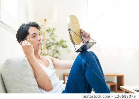 Young man putting on make-up in the living room 120692079