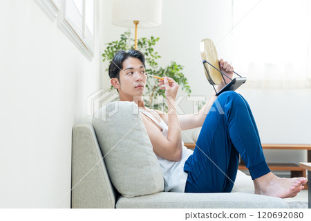 Young man putting on make-up in the living room Young man putting on make-up in the living room 120692080