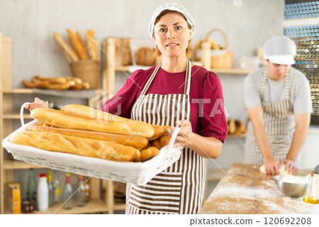Positive woman baker in uniform baking fresh baguettes in bakery 120692208