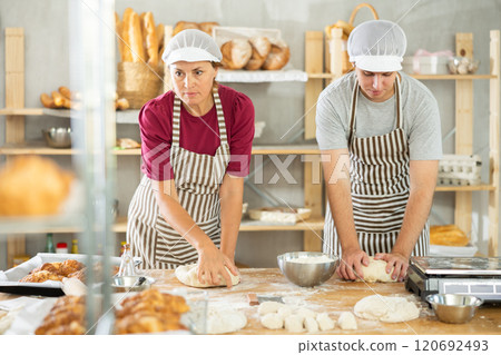 Two bakers, woman and young guy, knead raw dough on table in bakery kitchen 120692493
