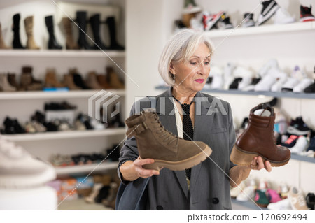 Elderly woman chooses boots in shoe store Elderly woman chooses boots in shoe store 120692494