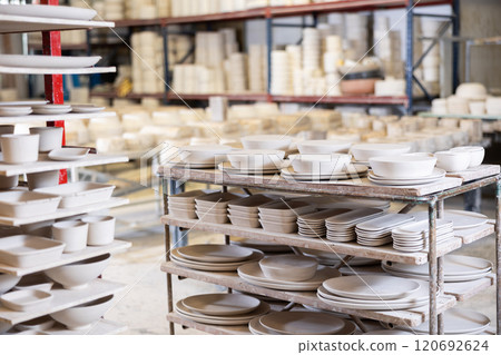 Raw slip cast pottery ready for kiln firing arranged on racks in workshop 120692624