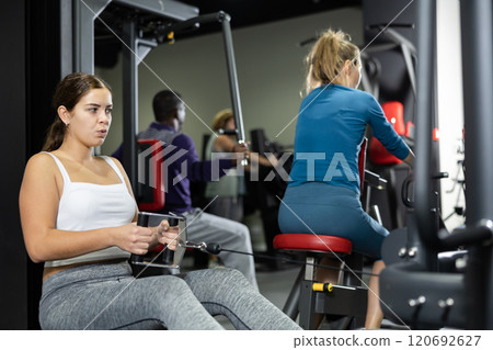 Caucasian woman doing exercises on cable row machine in gym 120692627