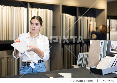 Girl carefully chooses ceramic tiles for her future apartment Girl carefully chooses ceramic tiles for her future apartment 120692629