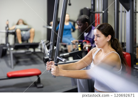 Sporty woman works on special simulator for development of pectoral muscles Sporty woman works on special simulator for development of pectoral muscles 120692671