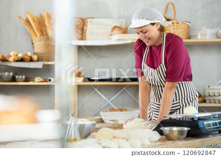 Adult female baker kneading dough on table Adult female baker kneading dough on table 120692847