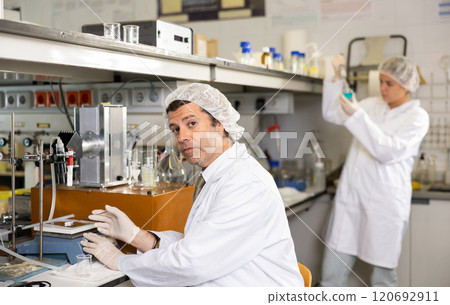 Latin middle-aged man chemist placing substance on stand for examination under microscope in lab 120692911
