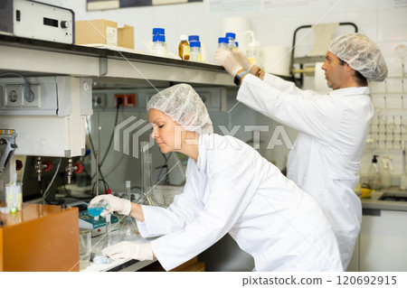 Concentrated man and woman chemists checking reagent in test tube during scientific research in modern laboratory 120692915