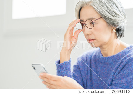 Senior woman looking at smartphone with reading glasses Senior woman looking at smartphone with reading glasses 120693110