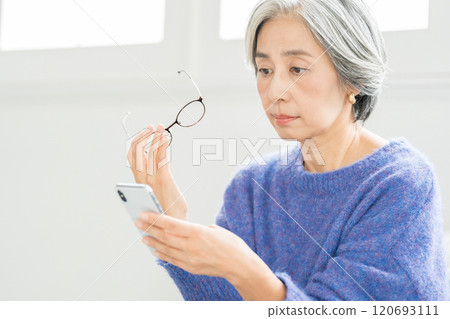 Senior woman looking at smartphone with reading glasses Senior woman looking at smartphone with reading glasses 120693111