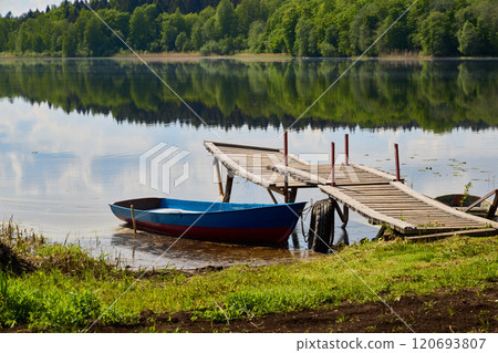 A picturesque and serene lakeside scene featuring a charming boat and a beautiful dock 120693807