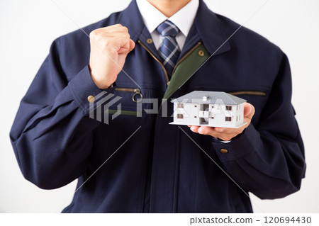 A middle-aged male businessman wearing navy blue work clothes making a fist pump while holding a model of an apartment building A middle-aged male businessman wearing navy blue work clothes making a fist pump while holding a model of an apartment building 120694430