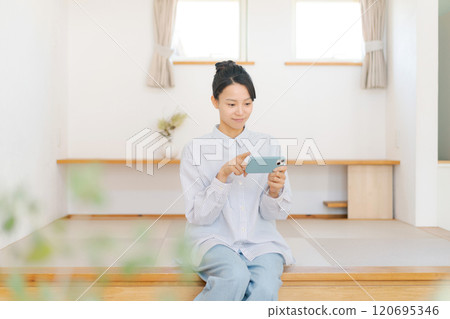 坐在榻榻米上看著智慧型手機的女人 120695346