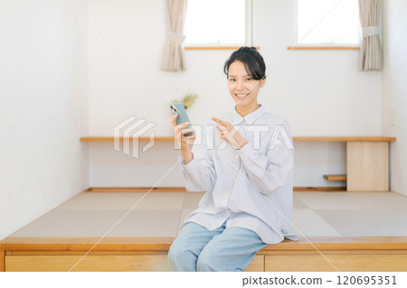 A woman sitting on a tatami mat and looking at her smartphone 120695351