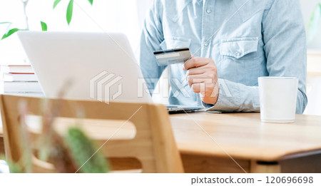 A man's hand looking at a credit card 120696698