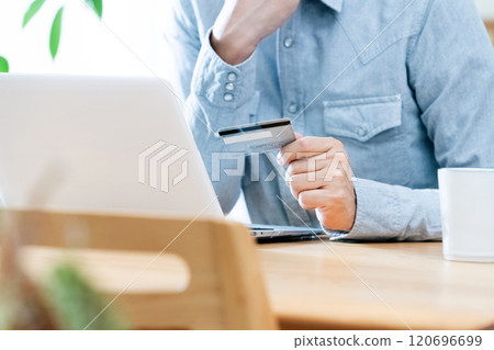 A man's hand looking at a credit card 120696699