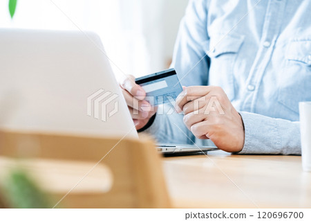A man's hand looking at a credit card 120696700