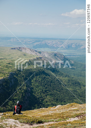 Male tourist resting and looking at the forest from the top of a mountain on a hike Male tourist resting and looking at the forest from the top of a mountain on a hike 120697346