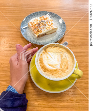 female holding yellow cup of coffee and near sweet pastry with fork on table . High quality photo 120697385