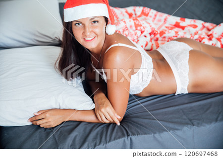 woman in lingerie on bed in bedroom near christmas tree with gifts woman in lingerie on bed in bedroom near christmas tree with gifts 120697468