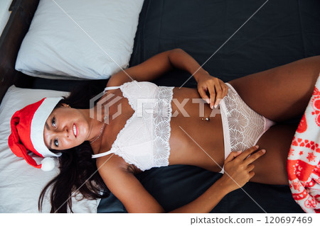 woman in lingerie on bed near christmas tree with gifts 120697469
