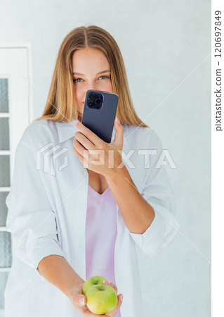 Beautiful woman holding a smartphone and two green apples Beautiful woman holding a smartphone and two green apples 120697849