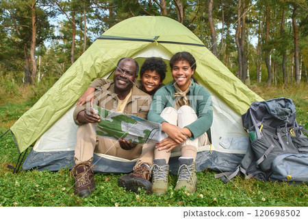 Portrait of African American family holding map and sitting in tent while posing for photo in forest Portrait of African American family holding map and sitting in tent while posing for photo in forest 120698502