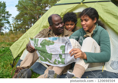 Medium close up of African American family reading map while resting in tent together Medium close up of African American family reading map while resting in tent together 120698504