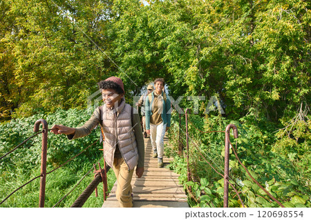 Curious African American boy going on wooden old bridge while his parent and older sister following him in background Curious African American boy going on wooden old bridge while his parent and older sister following him in background 120698554