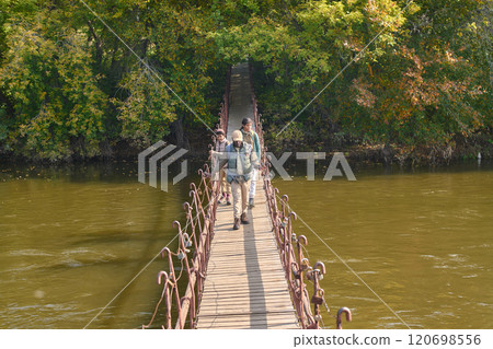 High angle shot of African American family with camping equipment going on wooden bridge over wide river in forest High angle shot of African American family with camping equipment going on wooden bridge over wide river in forest 120698556