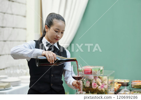 Pouring Red Wine into Glass at Formal Dining Setting 120699286