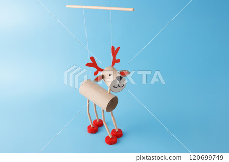 DIY reindeer puppet made from cardboard tubes, red bottle caps, and paper details. Festive paper craft marionette with red antlers. Holiday decoration and creative recycled materials project for kids, 120699749
