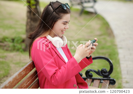 Smiling Woman with Headphones Using Smartphone Outdoors 120700423