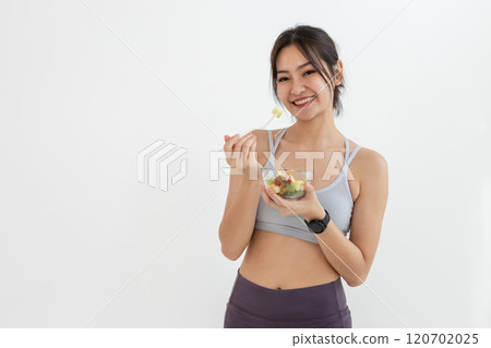 Asian attractive lady sportswear healthy eating salad vegetables over white background. Female holding salad bowl various vegetables and fruit healthy food for weight loss and exercise. Asian attractive lady sportswear healthy eating salad vegetables over white background. Female holding salad bowl various vegetables and fruit healthy food for weight loss and exercise. 120702025