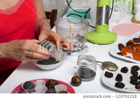 Woman makes candies from dried fruits. Balls of prunes, dates and coconut. With a sprinkle of black sesame powder. Woman makes candies from dried fruits. Balls of prunes, dates and coconut. With a sprinkle of black sesame powder. 120702228