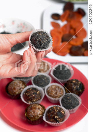 Woman puts dried fruit candies on a plate. Balls of prunes, dates and coconut. With a sprinkle of black sesame powder. Woman puts dried fruit candies on a plate. Balls of prunes, dates and coconut. With a sprinkle of black sesame powder. 120702246