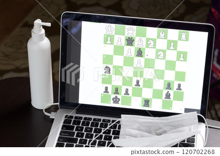 Chess task on laptop screen online. Near antibacterial spray and medical mask. Leisure in self-isolation. International chess day. Chess task on laptop screen online. Near antibacterial spray and medical mask. Leisure in self-isolation. International chess day. 120702268