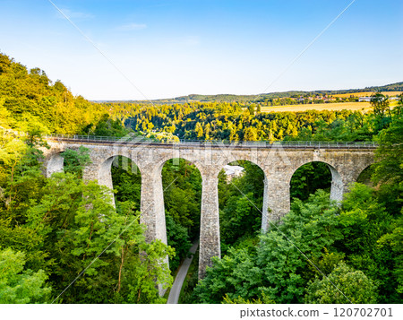 The Zampach stone railway bridge spans lush trees, showcasing impressive stone arches against a clear sky, set in the scenic Czech countryside. The Zampach stone railway bridge spans lush trees, showcasing impressive stone arches against a clear sky, set in the scenic Czech countryside. 120702701