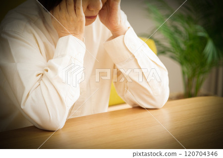 Middle-aged to senior woman holding her head in the living room Middle-aged to senior woman holding her head in the living room 120704346