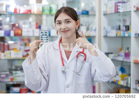 Woman pharmacist smiling holding blister pack at shelf stocked in pharmacy drugstore. Selecting type of medicine dispensing to patient. Woman pharmacist smiling holding blister pack at shelf stocked in pharmacy drugstore. Selecting type of medicine dispensing to patient. 120705692