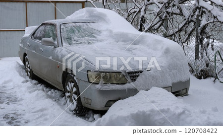 gray car covered with snow and half cleared in the yard of a private house against the background of grape vines, consequences for transport of heavy snowfall and snowstorm gray car covered with snow and half cleared in the yard of a private house against the background of grape vines, consequences for transport of heavy snowfall and snowstorm 120708422