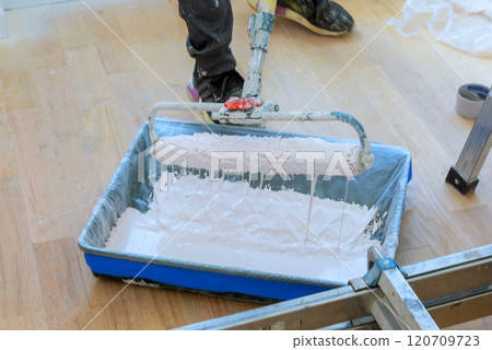 Person is using paint roller to apply fresh white paint from tray on paint for wall 120709723