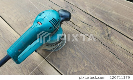A bright blue hand sander stands on brown and yellow textured wood with cracks. A bright blue hand sander stands on brown and yellow textured wood with cracks. 120711379