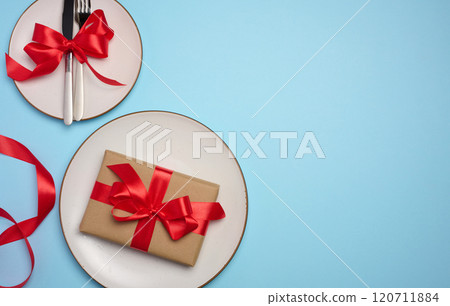 Round white plate and tied with red bow view with knife on a blue background, festive table setting 120711884