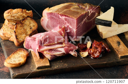 A piece of prosciutto, slices of ciabatta and cheese on a wooden board A piece of prosciutto, slices of ciabatta and cheese on a wooden board 120711907