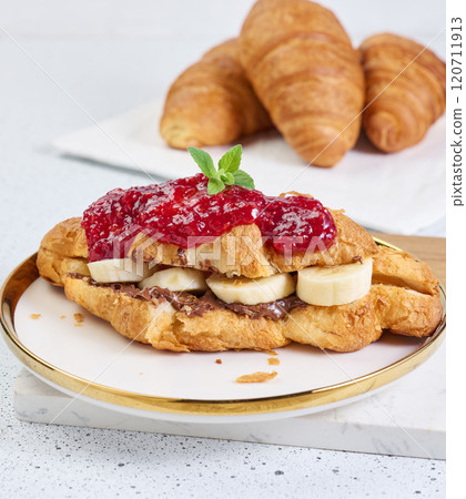 Croissant with banana pieces, chocolate paste in a round white plate Croissant with banana pieces, chocolate paste in a round white plate 120711913