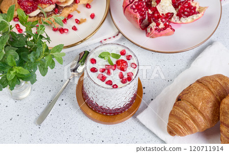 Glass of yogurt with chia seeds, pomegranate seeds and baked croissants on table Glass of yogurt with chia seeds, pomegranate seeds and baked croissants on table 120711914