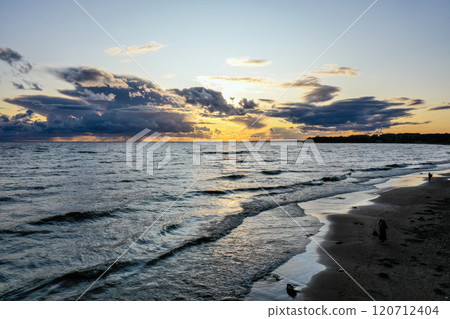 Tranquil sunset over the serene beach with gentle waves and dramatic clouds in the evening sky Tranquil sunset over the serene beach with gentle waves and dramatic clouds in the evening sky 120712404